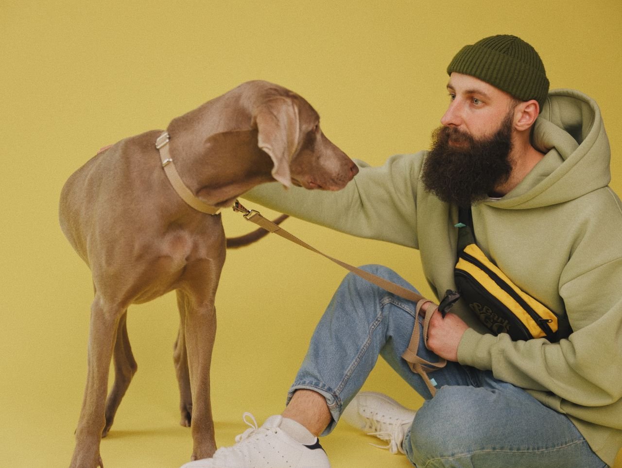 social-feed-img-01 A man with a beard in casual attire sits with his dog against a yellow background.